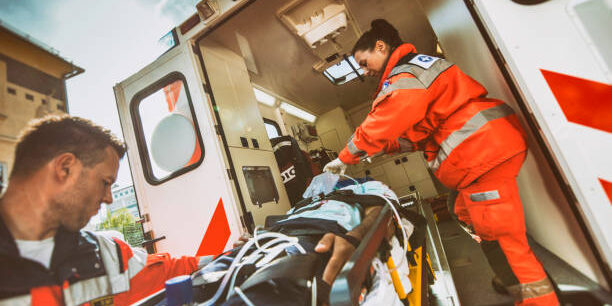 Paramedic team pushing stretcher with injured person towards ambulance.